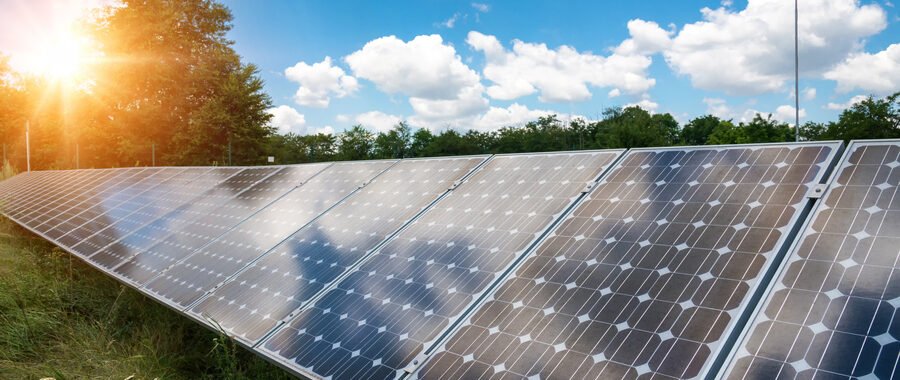 Assinatura de energia solar: painéis fotovoltaicos em destaque com verde ao fundo e nuvens